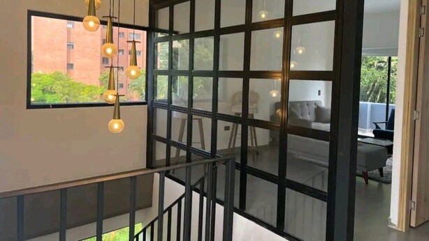 A modern interior with a staircase, a large window with a view of greenery, and hanging pendant lights. - 2 Floor PH in Provenza, Poblado - 4BR / 4Bath (Medellín)