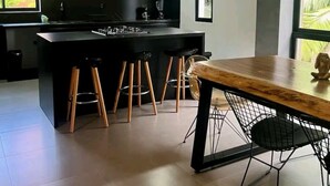 A modern kitchen with dark cabinetry, a central island with stools, and a dining area with a wooden table and metal chairs. - 2 Floor PH in Provenza, Poblado - 4BR / 4Bath (Medellín)
