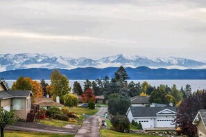 A residential street with houses, a driveway, and a lake with mountains in the background. - Stunning Lakeside House w/ Deck + Water Views (Lakeside)