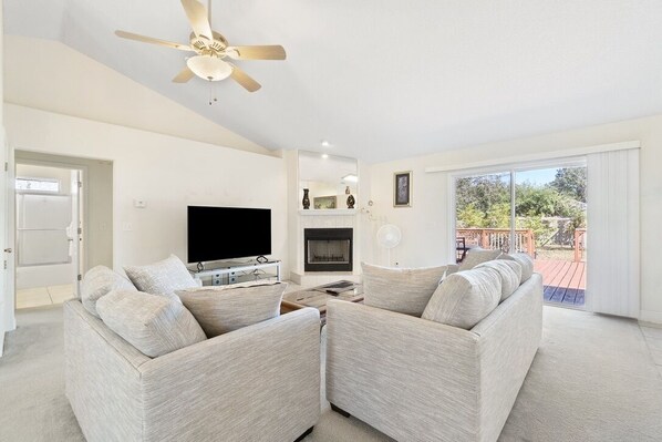 A modern living room with a flat-screen TV, a fireplace, and a balcony with a view of the outdoors.