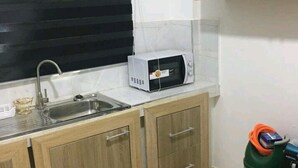 A small kitchenette with a sink, a microwave, and a trash bin. - Ajay's Residence for short and long stays. (Tema)