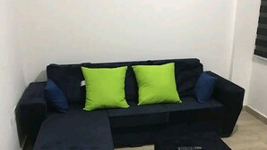 A living room with a dark-colored sofa, two bright green pillows, and a remote control on a small ottoman. - Ajay's Residence for short and long stays. (Tema)