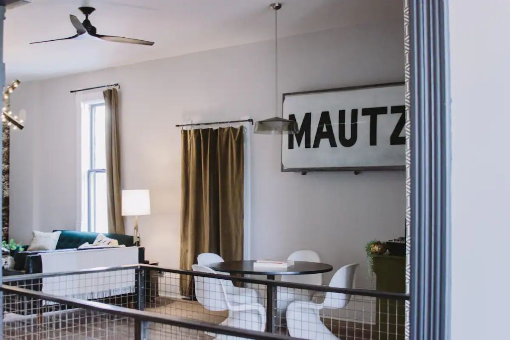 A modern hotel room with a bed, a desk, a chair, a dining table, and a large window with curtains.