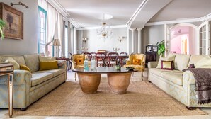 A spacious living room with a large round coffee table, two sofas, and a dining area with chairs. - Palace in the center of the town with pool (Sevilla)