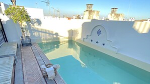 A rooftop swimming pool with a herringbone-patterned deck, a small seating area, and a clear view of the surrounding buildings. - Palace in the center of the town with pool (Sevilla)