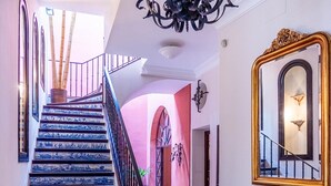 A grand staircase with blue-tiled steps leading to a landing. A chandelier hangs from the ceiling, and a large mirror is mounted on the wall. - Palace in the center of the town with pool (Sevilla)