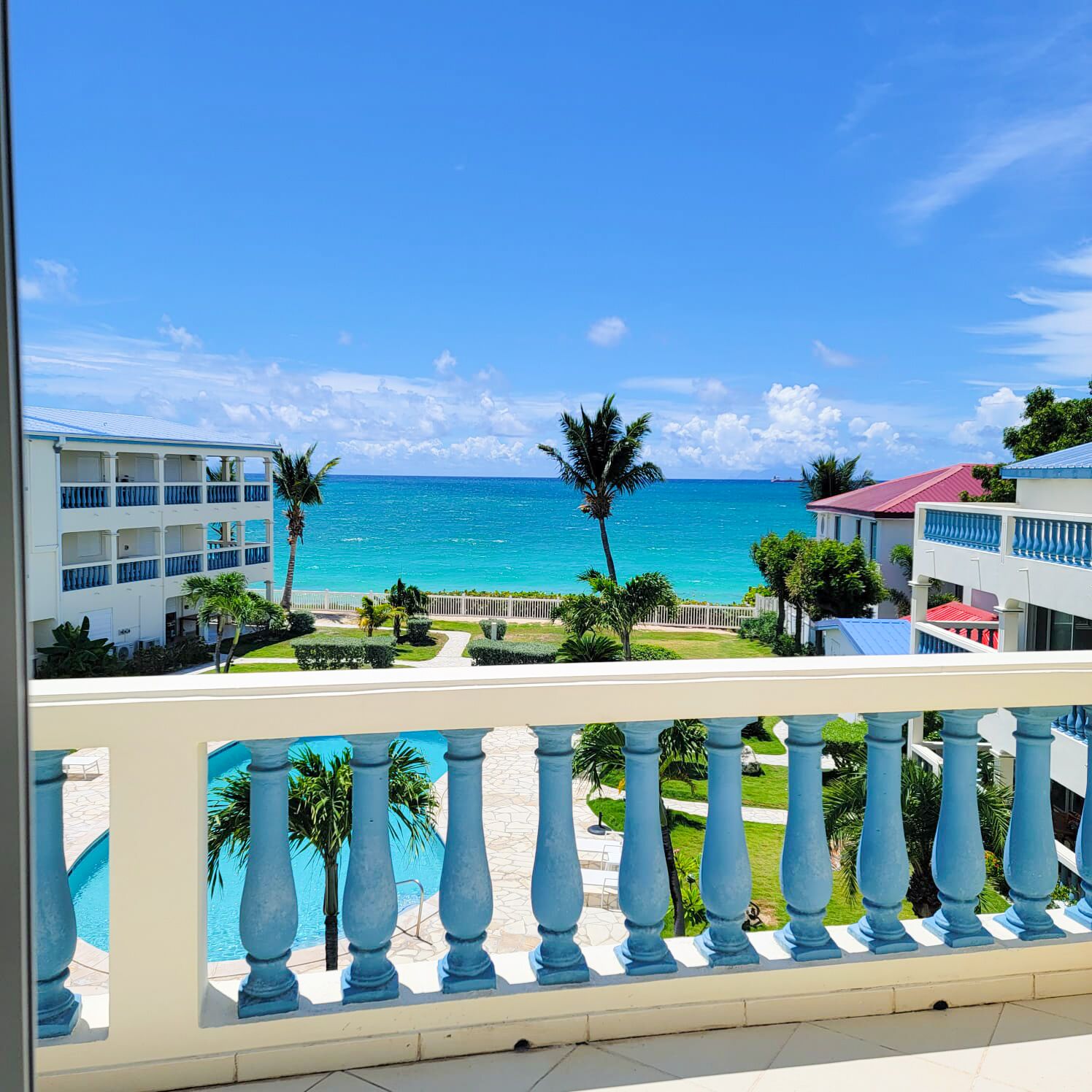 A hotel balcony with a view of the ocean and a pool.