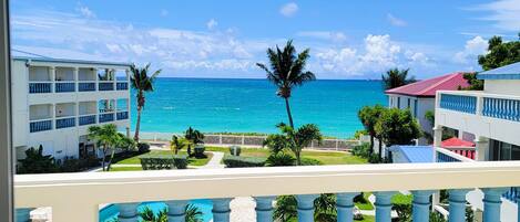 A hotel balcony with a view of the ocean and a pool.