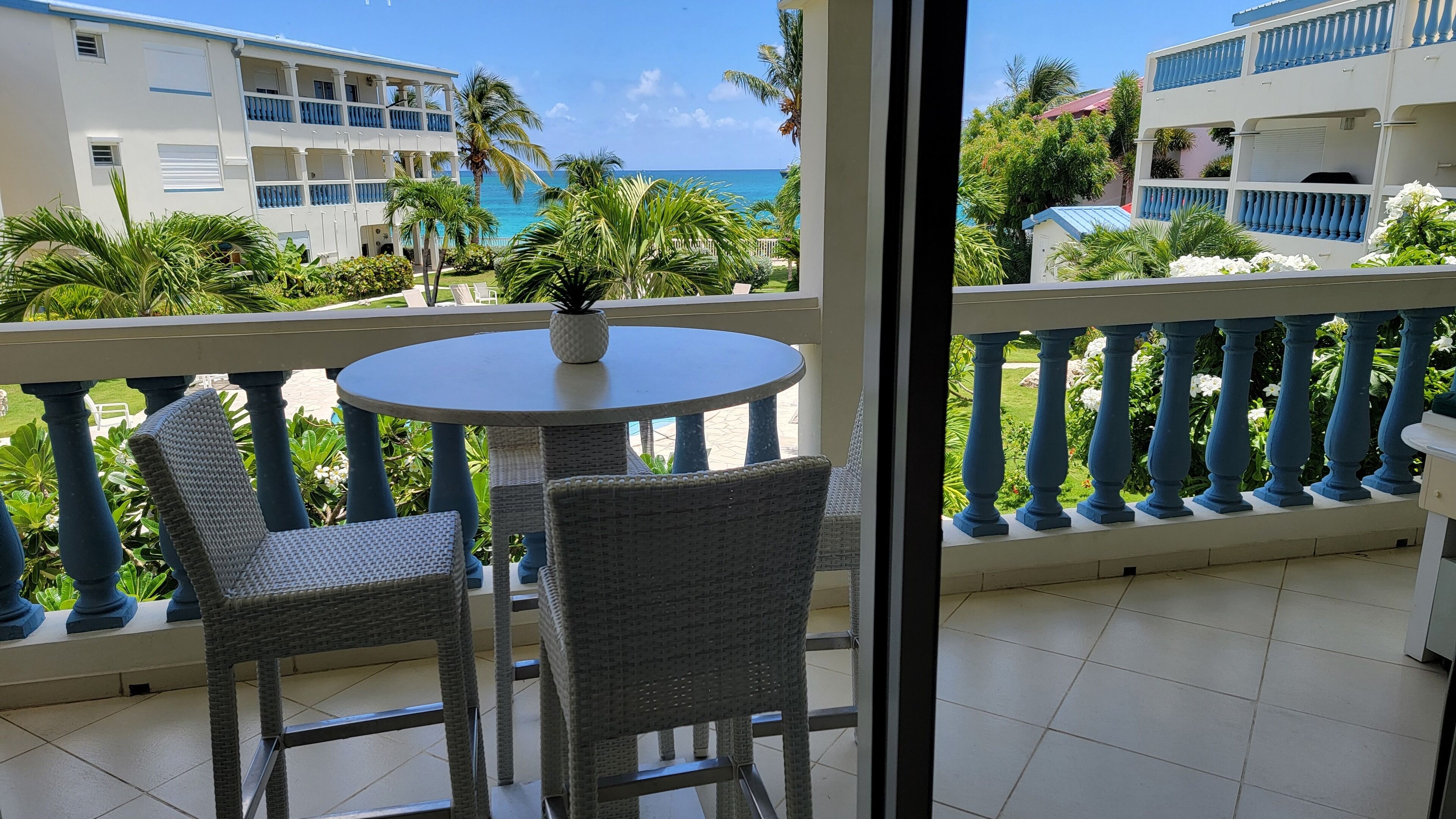 Uma varanda com cadeiras de vime e uma mesa, com vista para a praia e edifícios.