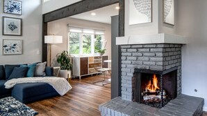 Una sala de estar moderna con chimenea de piedra, sofá azul oscuro y suelo de madera.