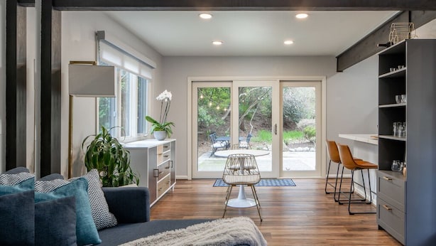 Una sala de estar moderna con un sofá, una mesa de comedor con sillas y una zona de cocina con una estantería.