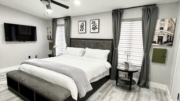 A modern bedroom with a large bed, a ceiling fan, a TV, and a small table with a vase.