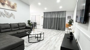 A modern living room with a sectional sofa, a round coffee table, and a flat-screen TV mounted on the wall.