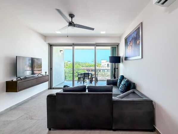 A modern living room with a sofa, a TV, a ceiling fan, and a balcony with a table and chairs.