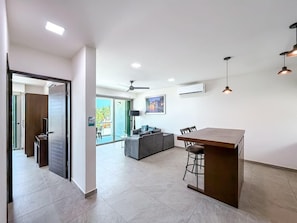 A modern kitchen with a dining area, a bar, and a living space with a sofa and a TV.