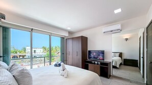 Ein Hotelzimmer mit einem großen Bett, einem Fernseher, einem Kleiderschrank und einem Balkon mit Blick auf Gebäude.