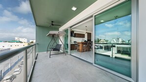 A balcony with a glass door leading to a kitchen area, a ceiling fan, and a view of the cityscape. - 2 BR Condo w/Ocean View Pool. Prime Location (Isla Mujeres)