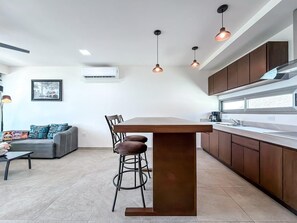 A modern kitchen with a central island, pendant lighting, and a dining area with a sofa and chairs.