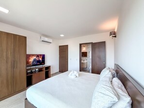A hotel room with a large bed, a TV, a wardrobe, and a bathroom visible through an open door.