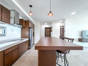 A modern kitchen with a central island, stainless steel appliances, pendant lighting, and a dining area with chairs.