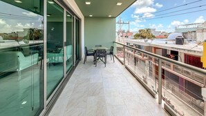 Un balcone con parete in vetro, un tavolo con sedie e vista sulla città.