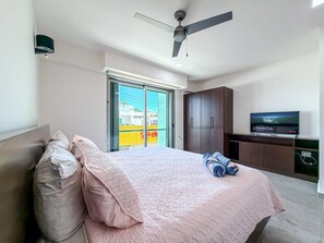 A bedroom with a bed, a ceiling fan, a TV, and a sliding glass door to the outside.