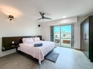 A bedroom with a bed, a ceiling fan, a sliding glass door to a balcony, and a wardrobe.