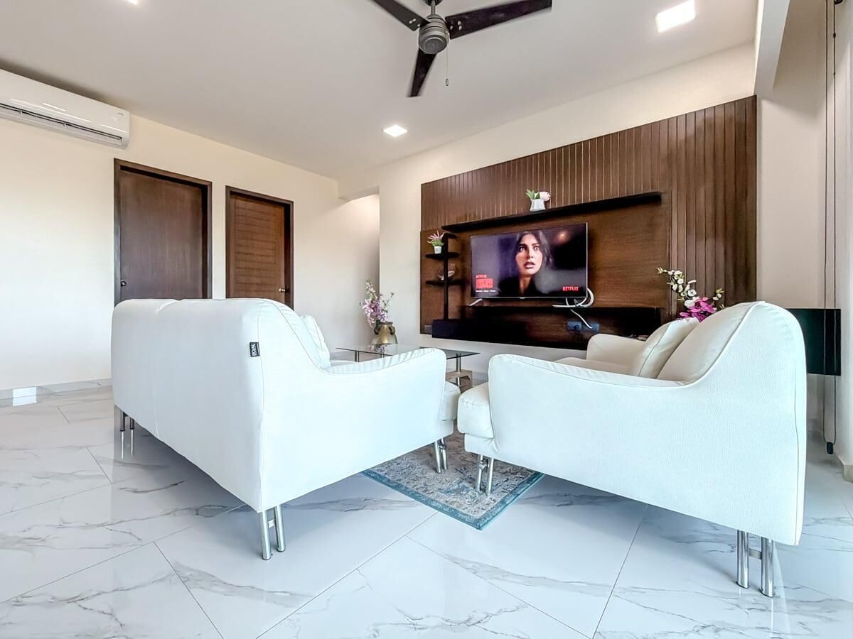 Una sala de estar moderna con un televisor de pantalla plana, sofás blancos, una mesa de centro y un ventilador de techo.