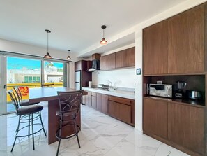 A modern kitchen with a bar area, wooden cabinets, and a view through large windows.