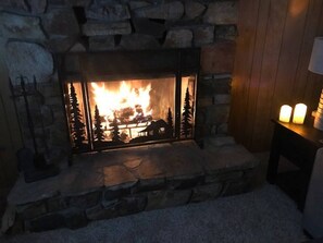 A stone fireplace with a fire, a small table with candles, and a wooden wall.