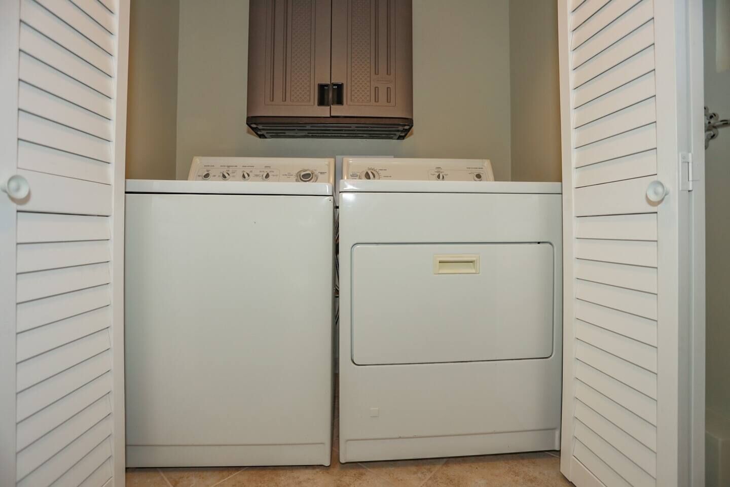 Une buanderie équipée de deux lave-linge et deux sèche-linge à chargement frontal, tous deux de couleur blanche, avec un meuble en bois au-dessus et une porte dotée d'une poignée.