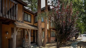 A row of two-story wooden buildings with balconies, a covered porch, and a tree with red leaves. - Kuma Lodge, 1 Night Free! (Big Bear Lake)