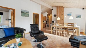 A modern living room with a leather sofa, a black leather chair, a wooden coffee table, and a dining area with wooden chairs and a brick wall. - Lovely home in Fjerritslev with WiFi (Fjerritslev)