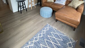 A modern kitchen with a central island, a brown leather sofa, and a blue ottoman. - Wine, Lake, Repeat I City Edge Retreat Naramata Wine Gateway (Penticton)