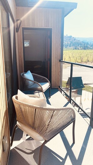 A balcony with wicker chairs and a table, overlooking a vineyard.