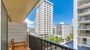 A balcony with a wooden bench, overlooking a cityscape with tall buildings and a clear sky. - Waikiki Studio with Balcony & incredible pool Sleeps 3 (Honolulu)