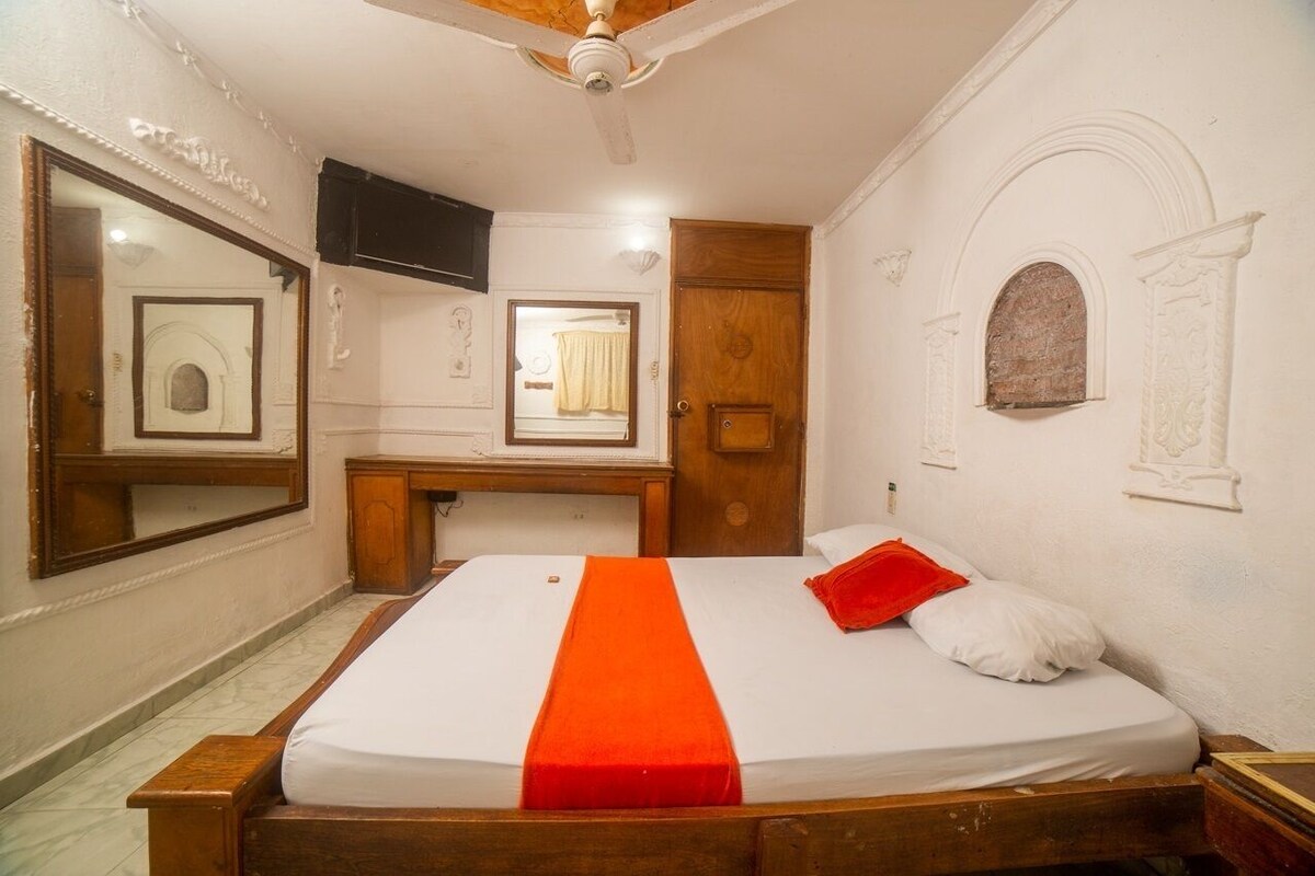 A bedroom with a bed, a desk, a mirror, and a television.