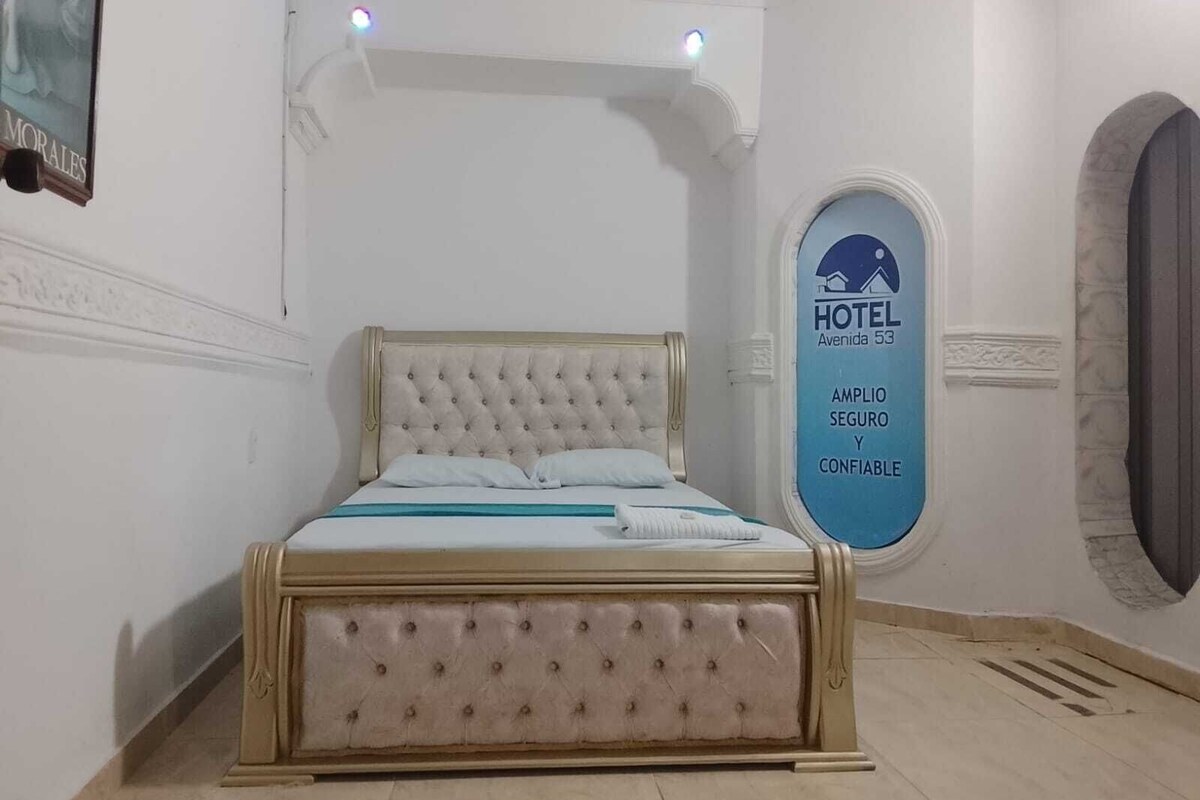 A bedroom with a large bed, a wall-mounted TV, and a sign indicating the hotel name and amenities.