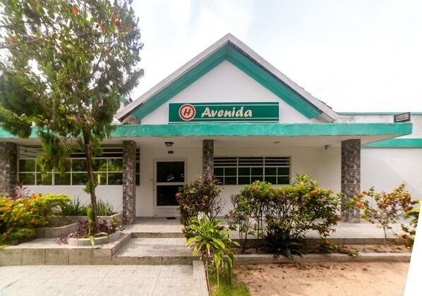 A building with a green and white facade, a sign reading "Avenida," and a landscaped entrance with steps and plants. - Hotel avenida 53 (Barranquilla)