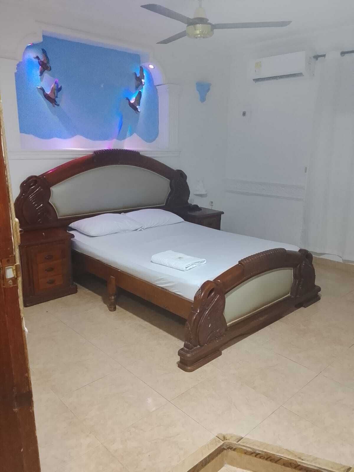 A bedroom with a wooden bed, a nightstand, a ceiling fan, and a wall-mounted TV.