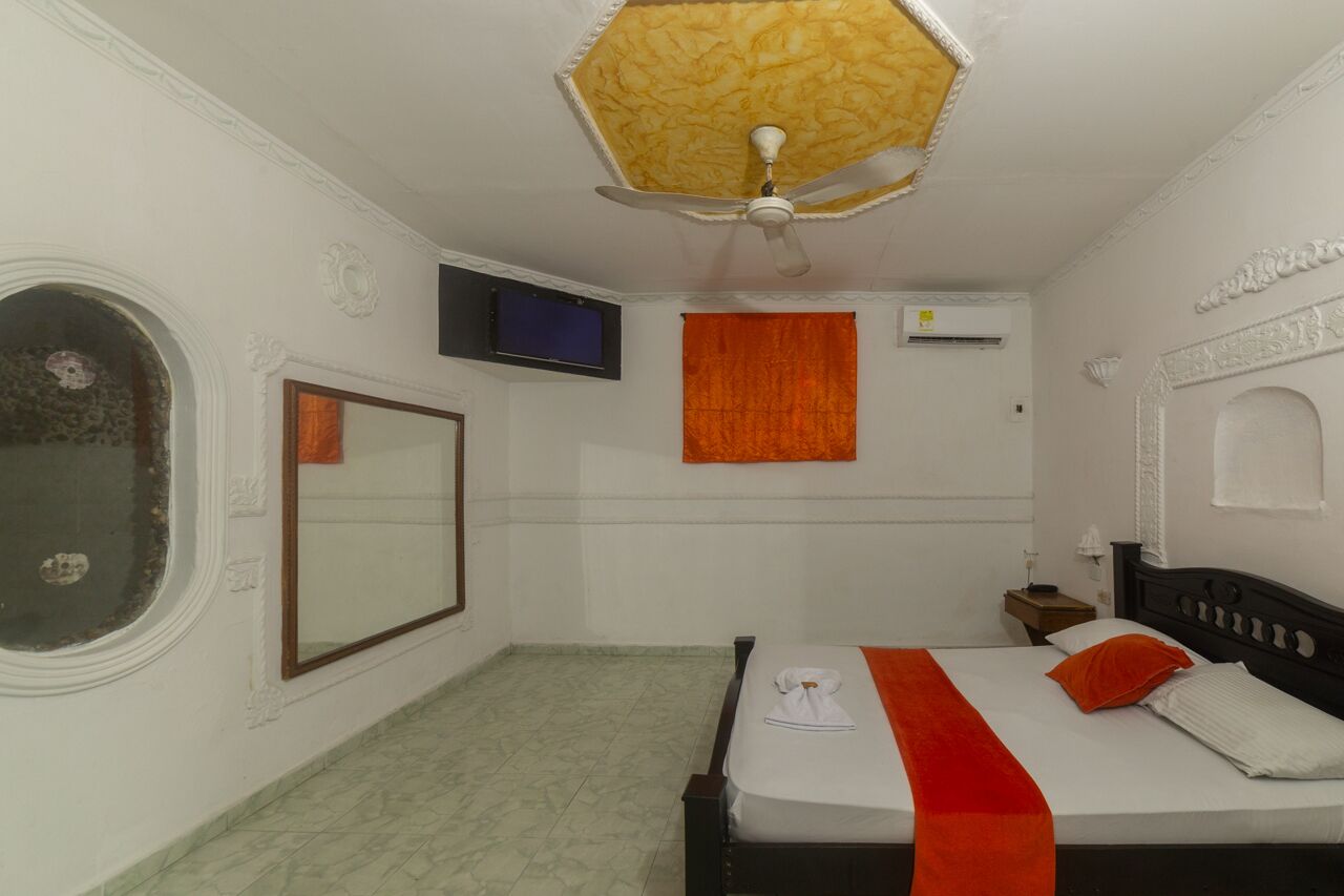 A hotel room with a bed, a television, a window with a curtain, and a ceiling fan.