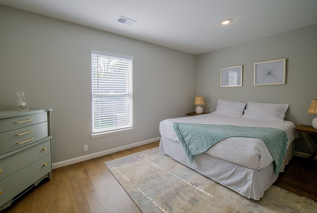 Une chambre à coucher comprenant un lit, une commode, une fenêtre avec des stores et deux lampes fixées au mur.