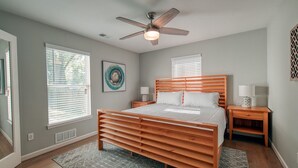A bedroom with a wooden bed, two bedside tables, a ceiling fan, and large windows with blinds.