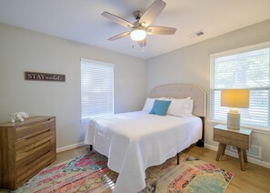 Ein Schlafzimmer mit Bett, Deckenventilator, Kommode, Nachttisch und Teppich.
