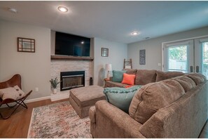 Cozy living room with a fireplace, sofa, and side table, featuring a window with blinds and a decorative mirror.