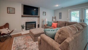 A living room with a fireplace, a large sofa, a rocking chair, and a television mounted above the fireplace.