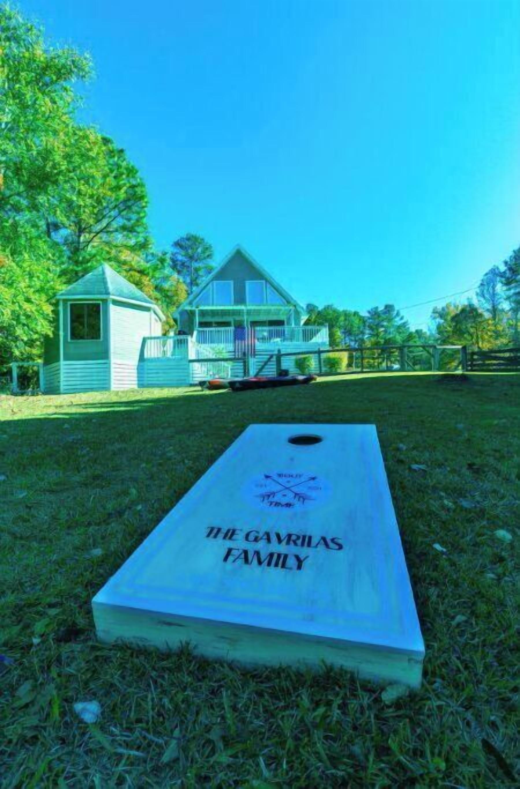 A wooden board with "THE GAVRILAS FAMILY" written on it, placed on grass in front of a house with a porch.