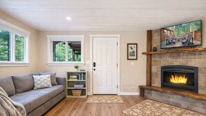 A cozy living room with a fireplace, a sofa, a bookshelf, and a door leading to a deck.