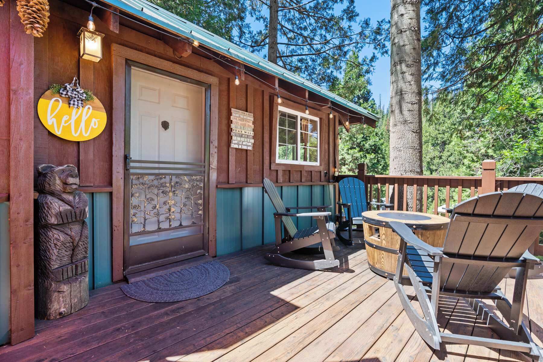 A wooden cabin with a porch, a welcome sign, a bear sculpture, and a sign with motivational phrases.