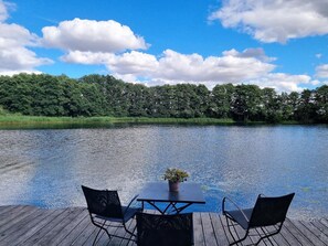 Relax on the deck overlooking the calm water, surrounded by lush greenery.